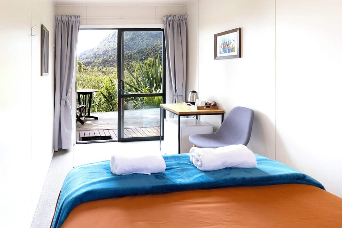 Habitación de hotel con cama, una silla, una mesa y vistas a zonas verdes y montañas a través de una puerta corredera.