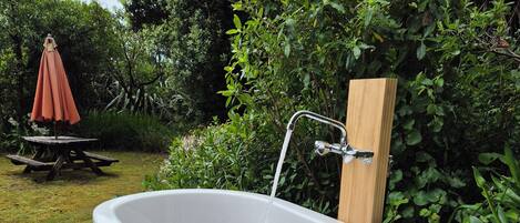 Eine freistehende Badewanne in einer Außenanlage mit einer Holzterrasse und einem Picknicktisch im Hintergrund.