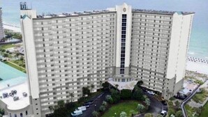 Un hotel grande y de varios pisos, con una torre central, un estacionamiento y vista al océano.