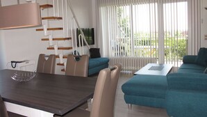 Een moderne woonkamer met een eethoek, een trap en grote ramen.