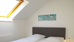 Een slaapkamer met dakraam, een bed met wit beddengoed, een nachtkastje met een lamp en een schilderij aan de muur.