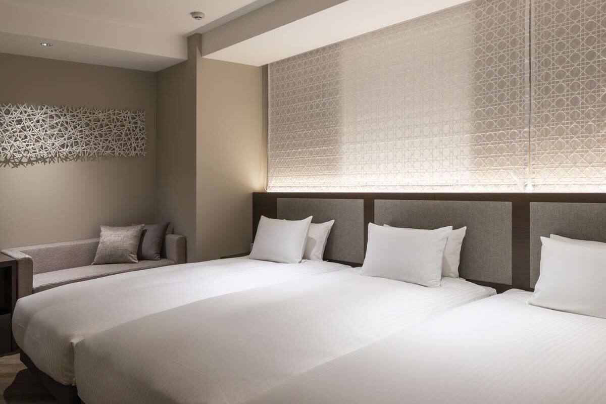 A hotel room with two large beds, a sofa, and a decorative wall panel.