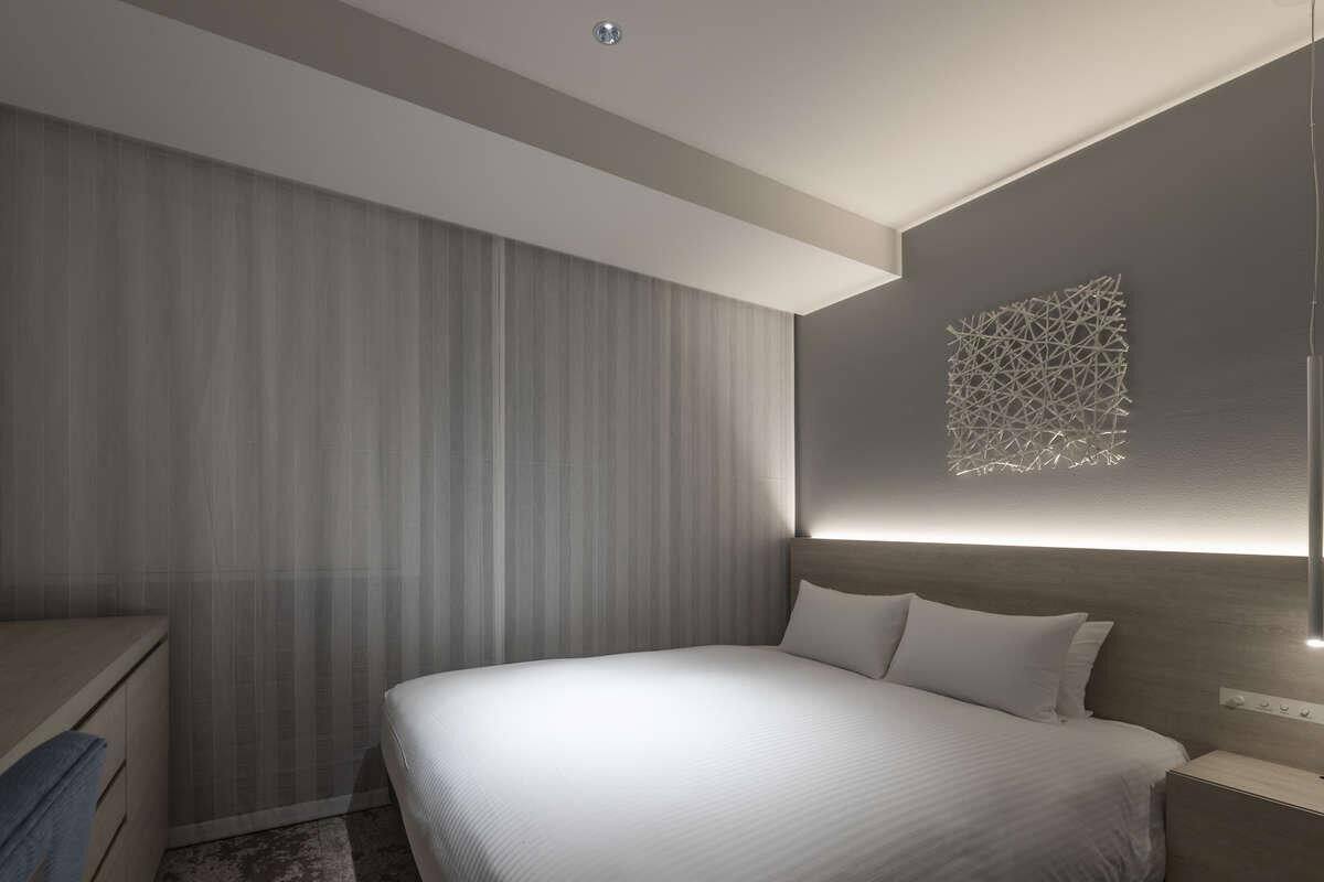 A modern hotel room with a large bed, a bedside table, and a wall-mounted light fixture.