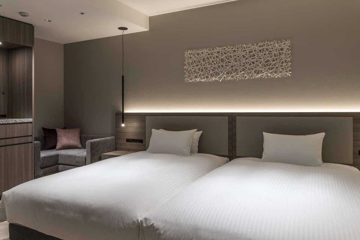 A modern hotel room with a large bed, a seating area with a chair, and a decorative wall piece.