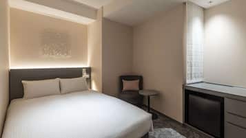 A hotel room with a large bed, a small desk, a chair, and a window with curtains.