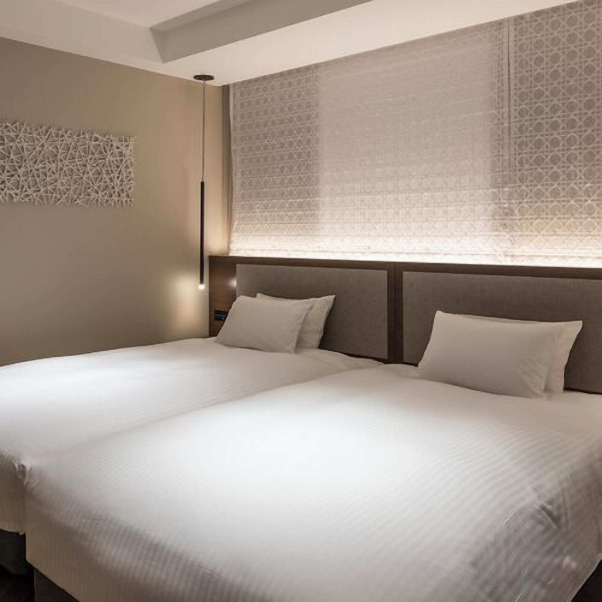 Una cama doble con cabecera, una lámpara fijada a la pared y una persiana con diseño.