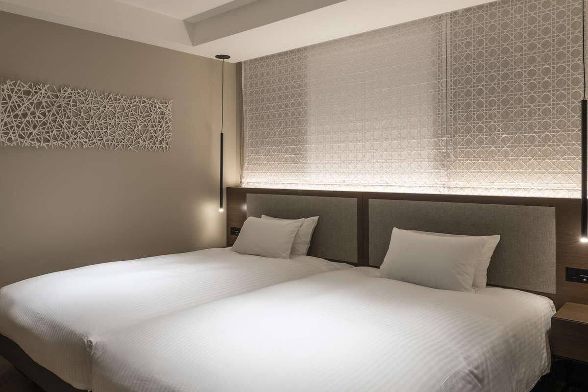 A double bed with a headboard, a wall-mounted light, and a window with patterned curtains.