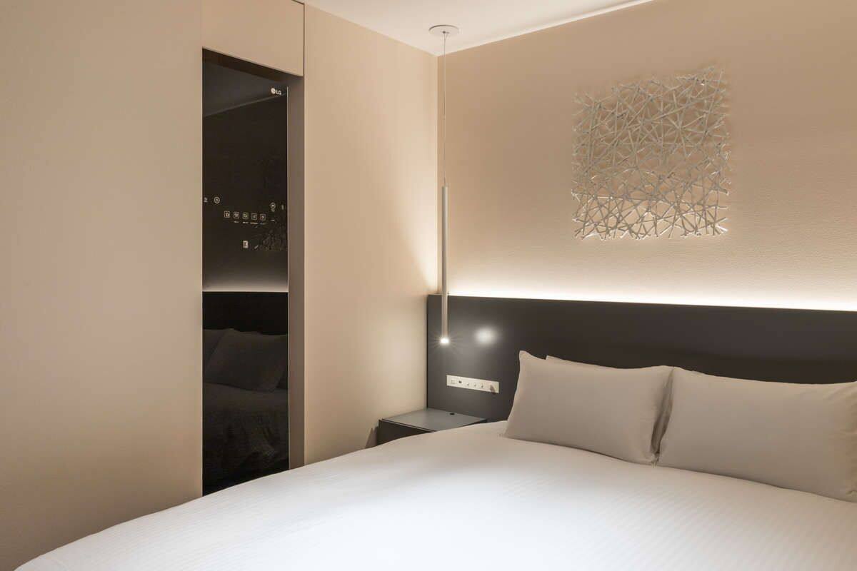 A hotel room with a large bed, a nightstand, a wall-mounted light, and a closet with a mirror.