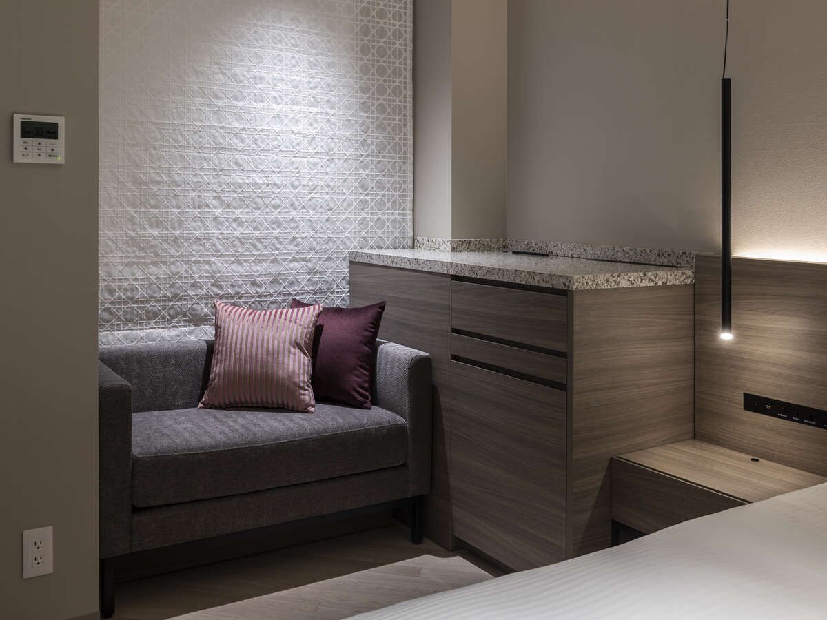 A modern bathroom with a grey sofa, a wooden vanity, and a textured wall.