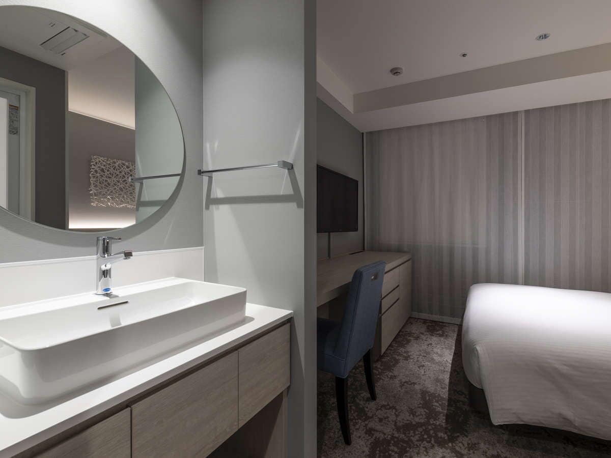 A modern hotel room with a large white sink, a mirror, a flat-screen TV, a desk, and a bed.