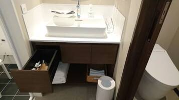 A bathroom with a white sink, a mirror, a towel rack, a trash bin, and a cabinet with drawers.