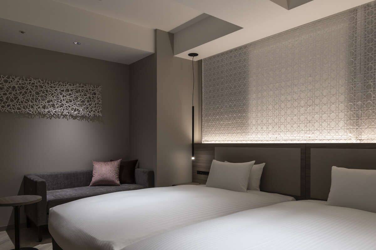 A modern hotel room with a large bed, a sofa, a small table, and a decorative wall piece.