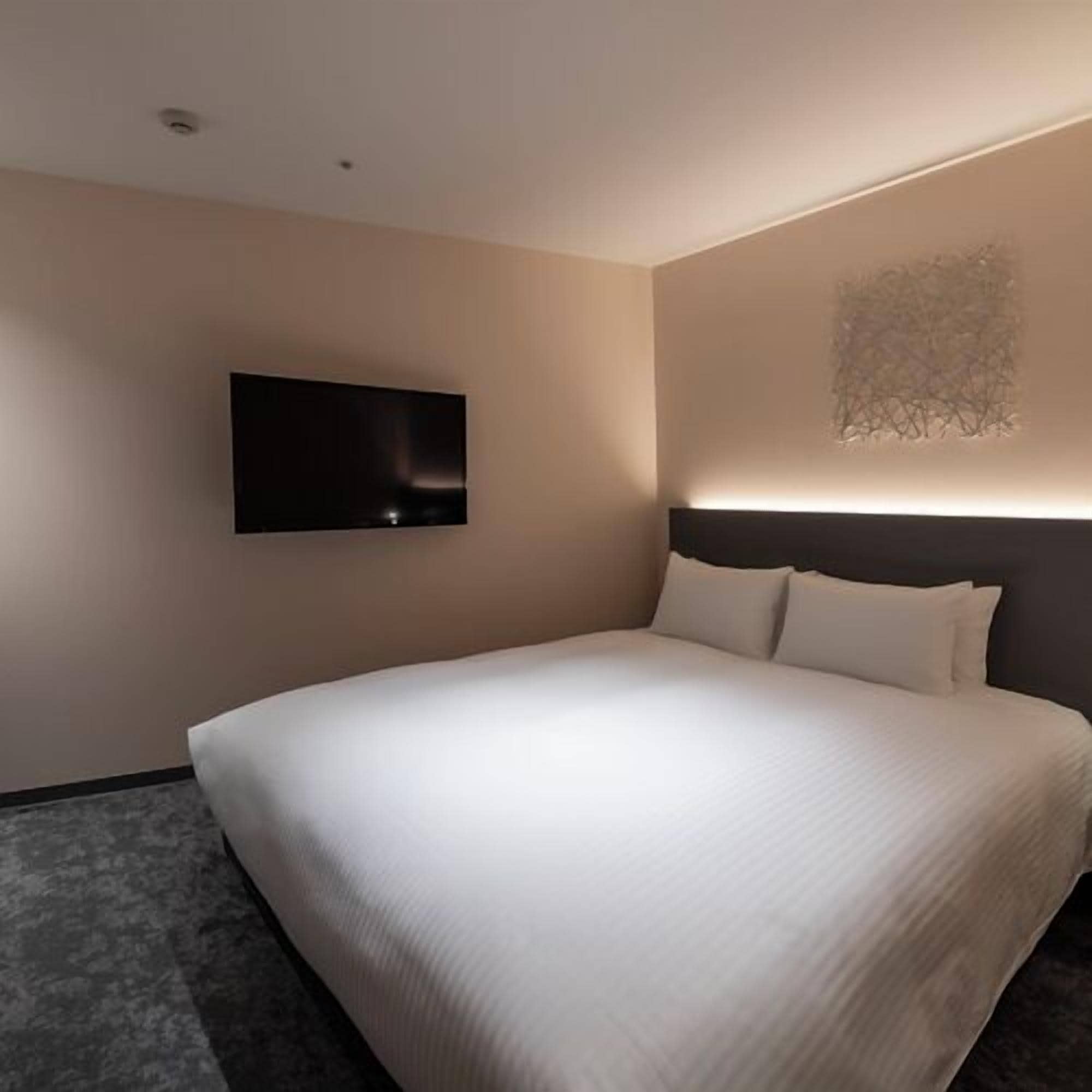 Una habitación de hotel moderna con una cama grande, un televisor de pantalla plana en la pared y una original obra de arte en la pared.