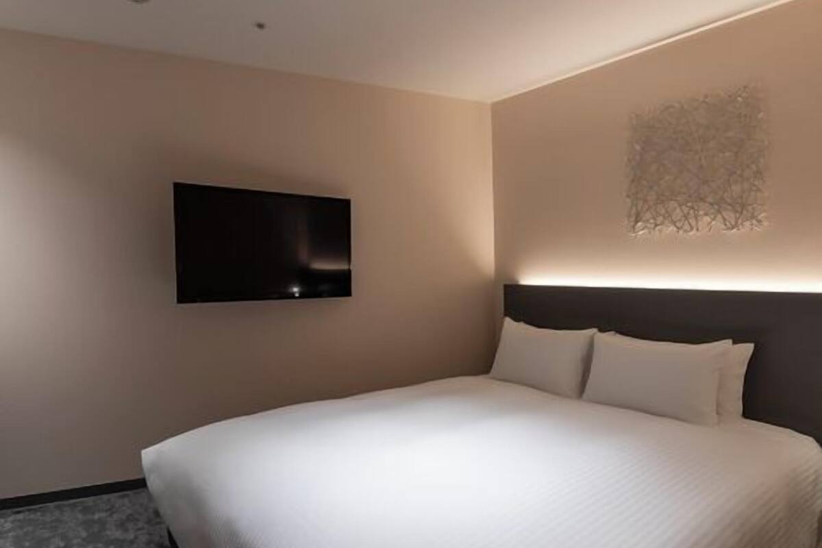 A modern hotel room with a large bed, a flat-screen TV mounted on the wall, and a unique wall art piece.