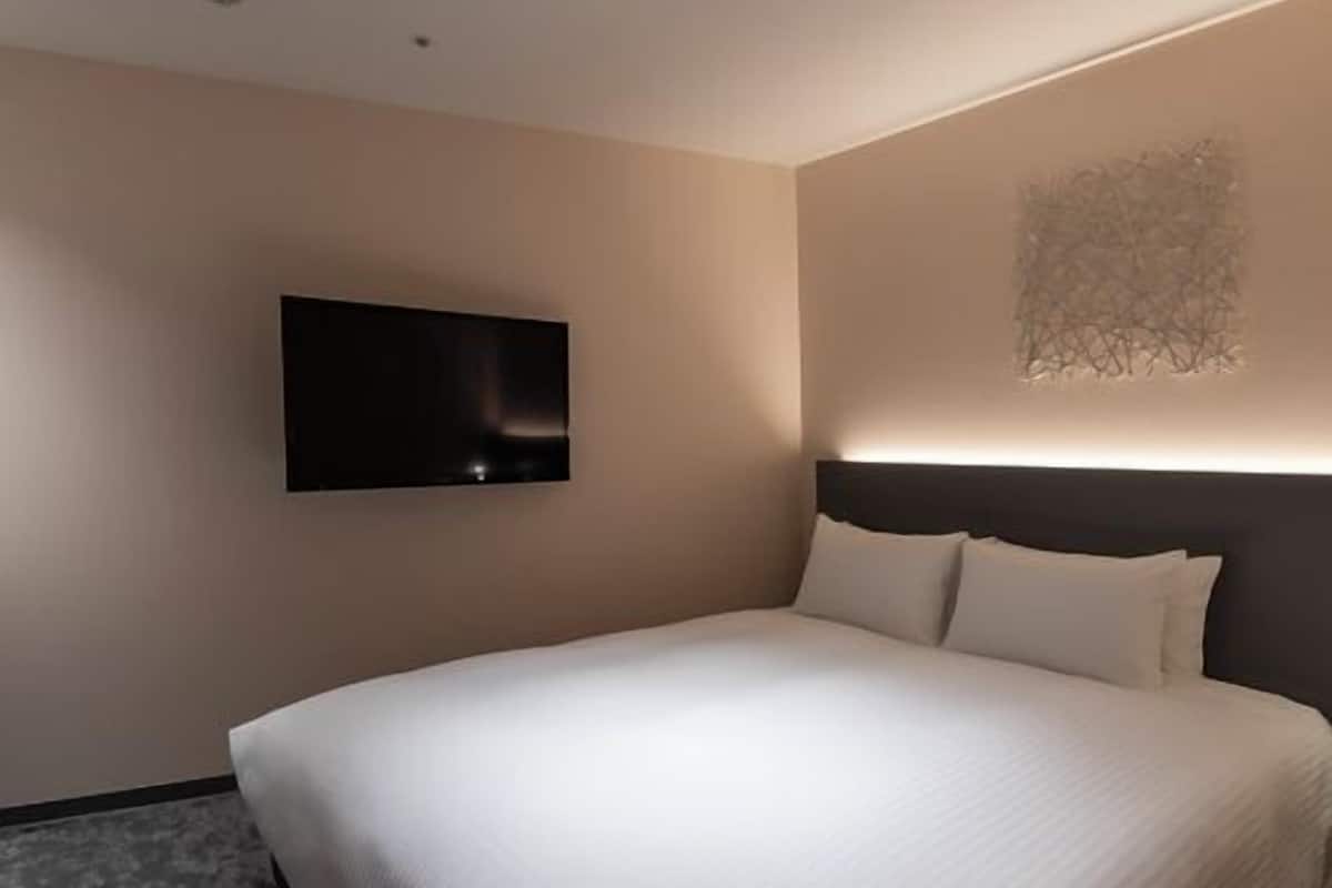 A modern hotel room with a large bed, a flat-screen TV mounted on the wall, and a unique wall art piece.