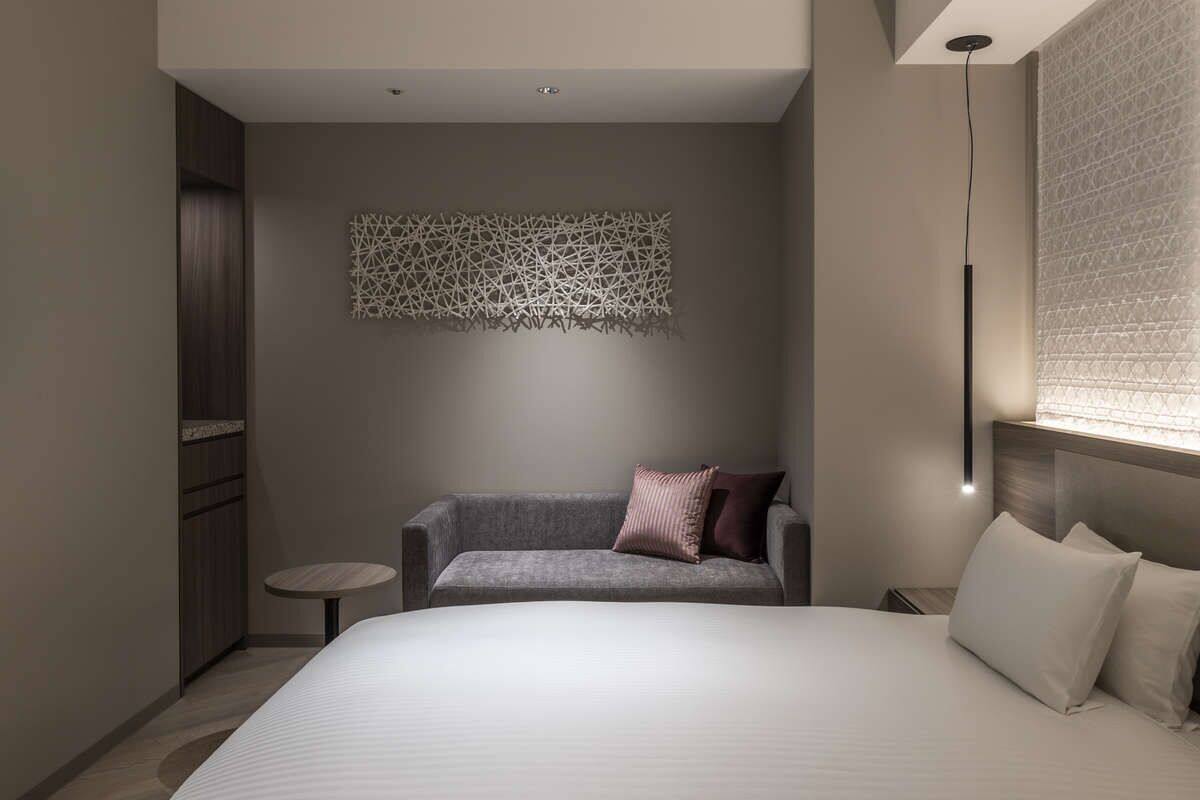 A modern hotel room with a large bed, a small sofa, a round table, and a decorative wall piece.