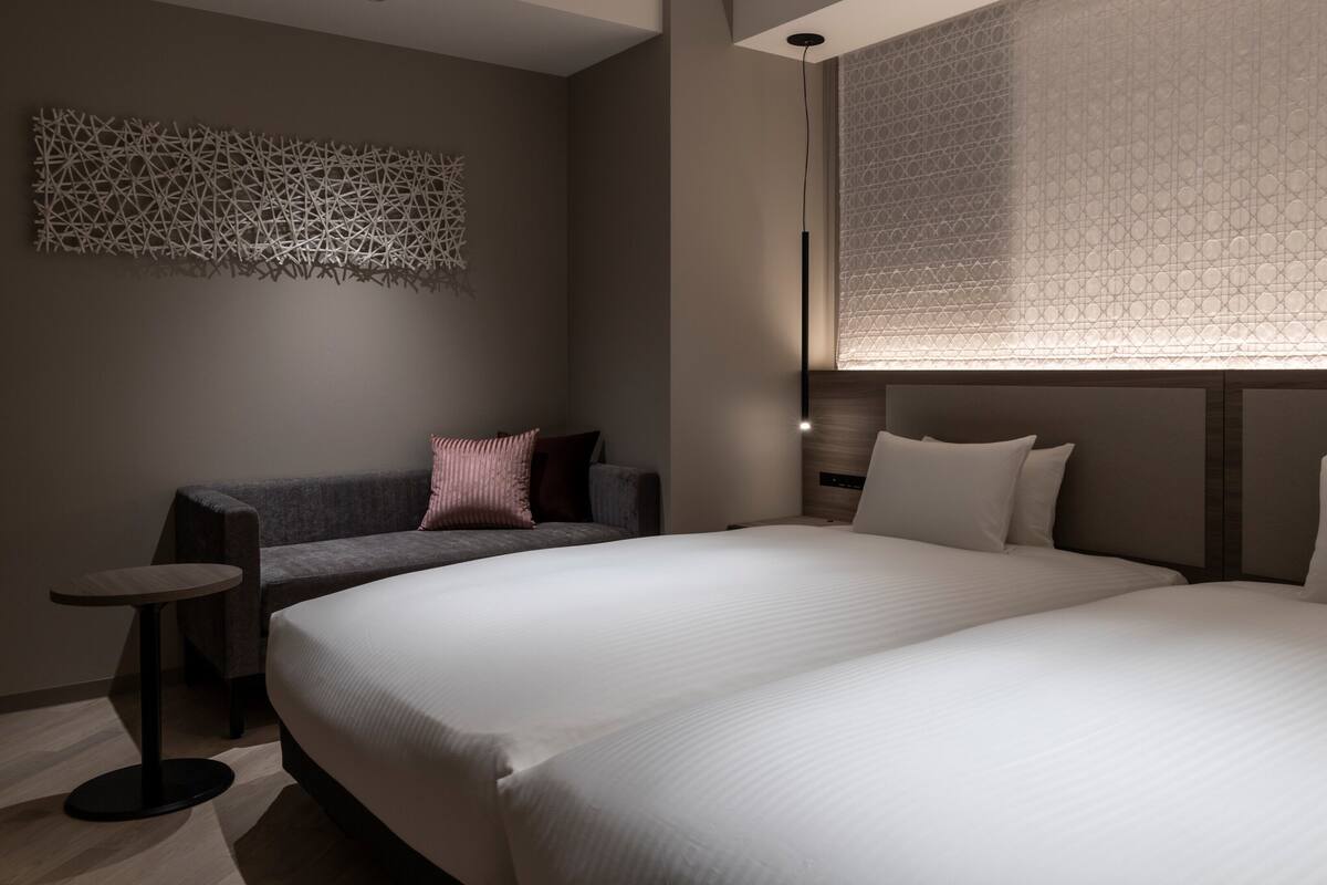 A modern hotel room with a large bed, a sofa, a small table, and a decorative wall piece.
