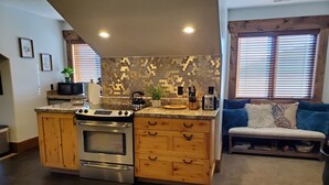 A modern kitchen with wooden cabinets, a built-in oven, and a granite countertop. There is a seating area with a blue sofa and a rug. - LUXURY Loft on Multi-Million 4 acre Estate in charming, Swiss town (Midway)