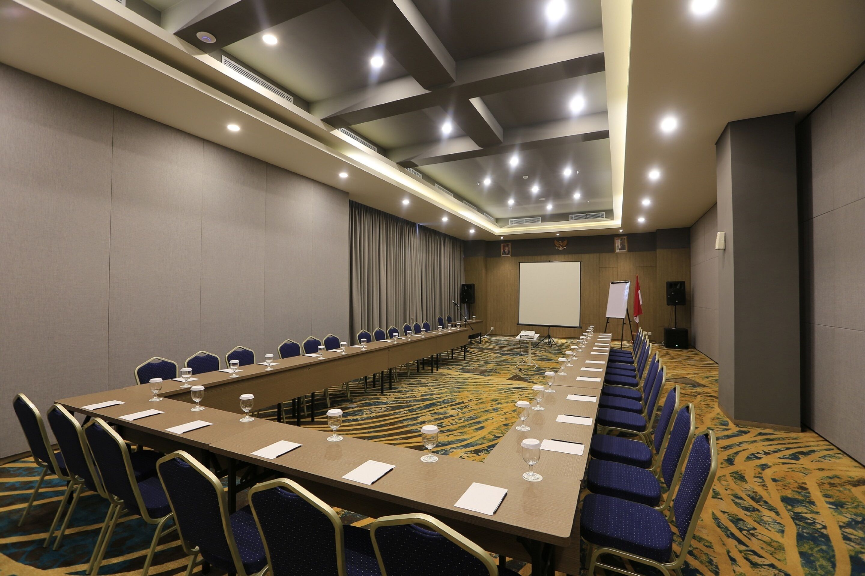 A conference room with a long table, chairs, and a projector screen.
