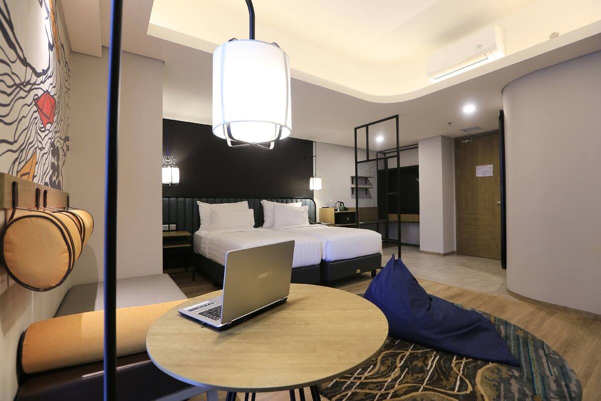 Una habitación de hotel moderna con una cama, un ordenador portátil sobre una mesa redonda, un sofá y una alfombra estampada.