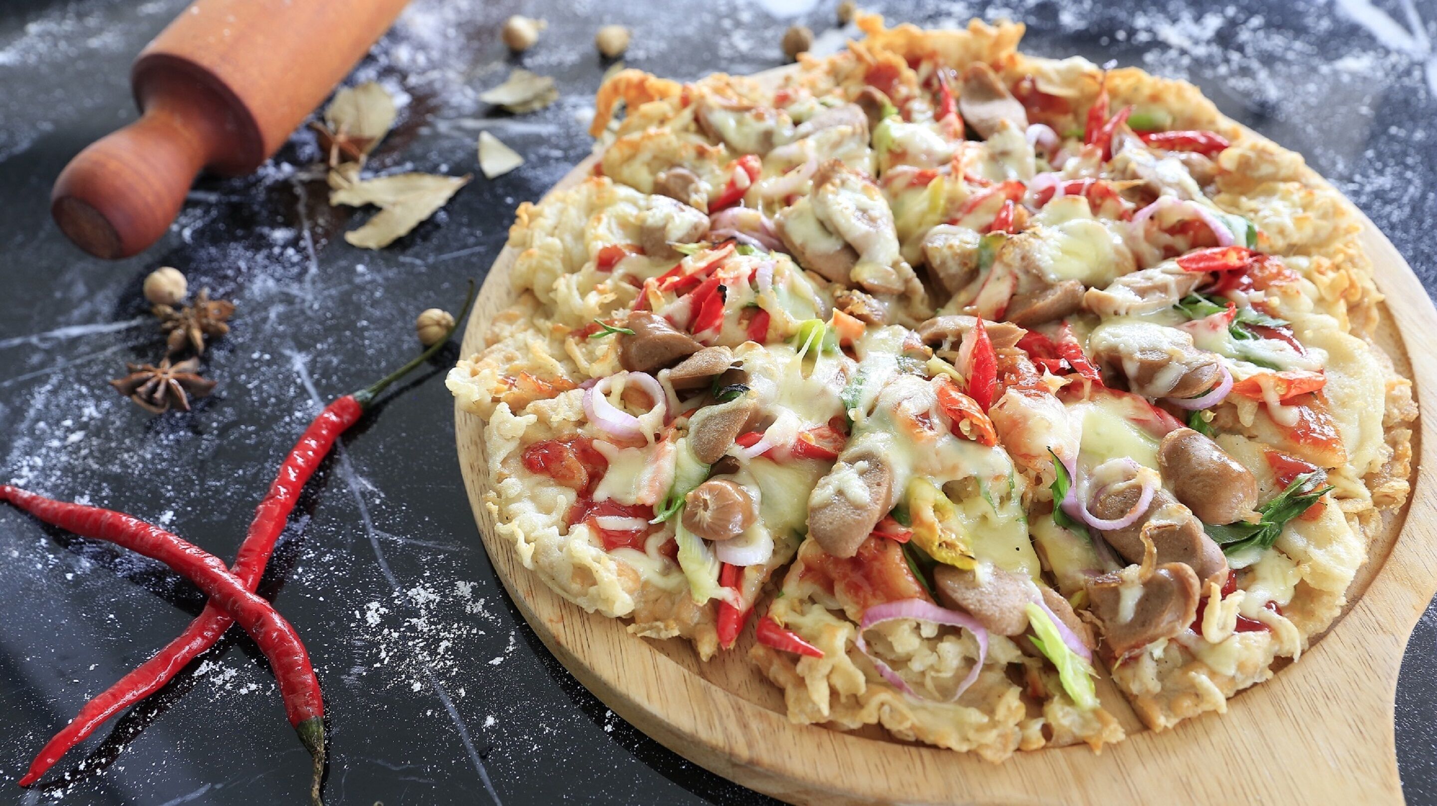 Pizza op een houten plank, met een deegroller en kruiden in de buurt.