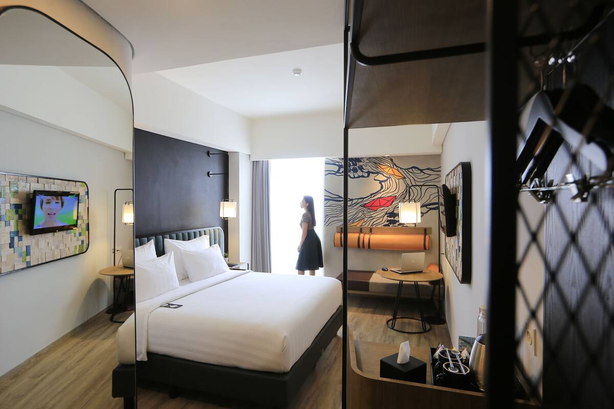 Habitación de hotel con una cama grande, un escritorio, un televisor y vistas al pasillo.