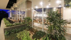 Un espace jardin intérieur aménagé avec des sièges et offrant une vue sur un restaurant ou un café grâce à des murs en verre.