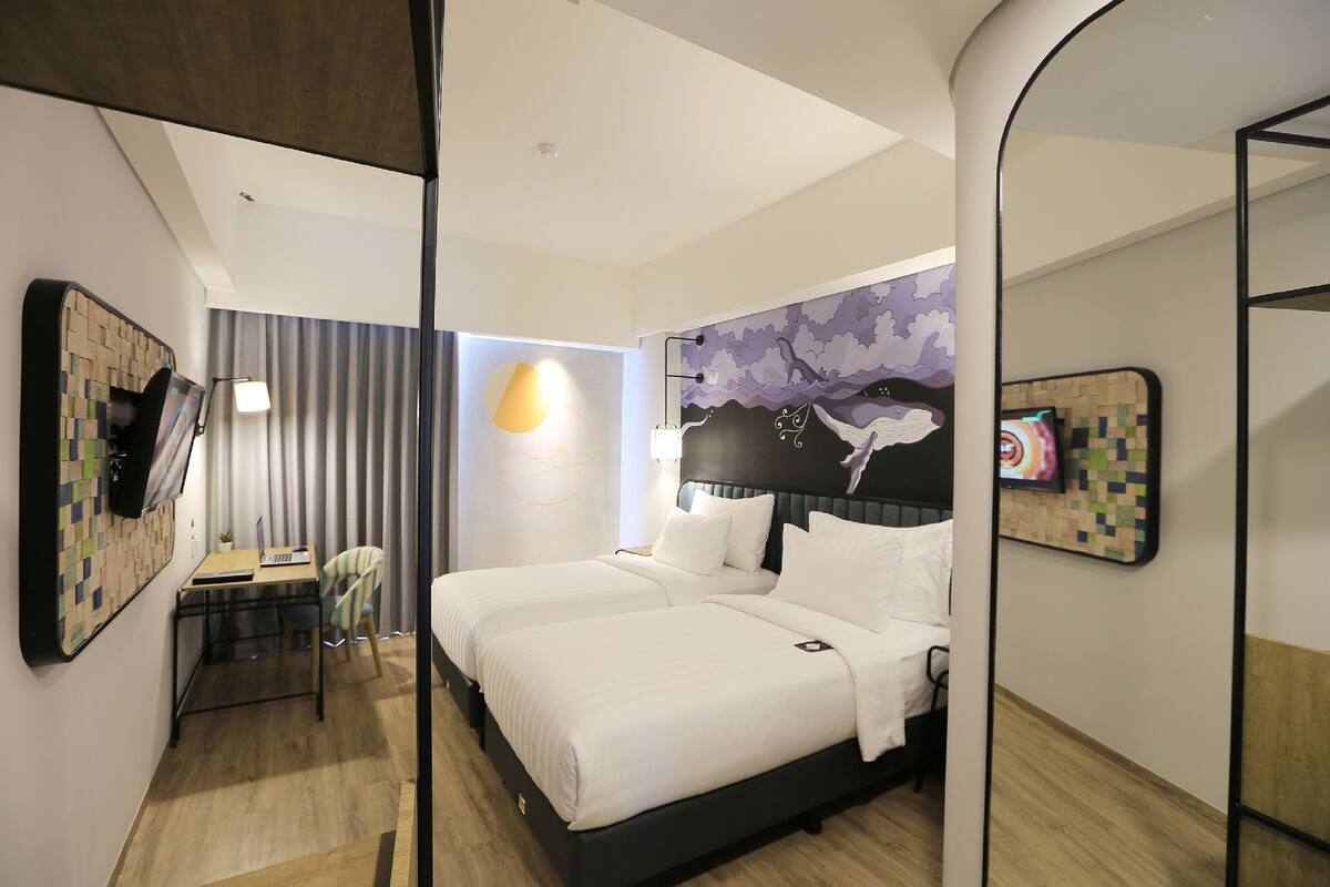 Habitación de hotel con cama, escritorio, silla y televisor montado en la pared.