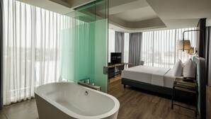 Une chambre d’hôtel moderne dotée d’une grande baignoire, d’un lit, d’une télévision et offrant une vue sur la ville grâce à de grandes fenêtres.