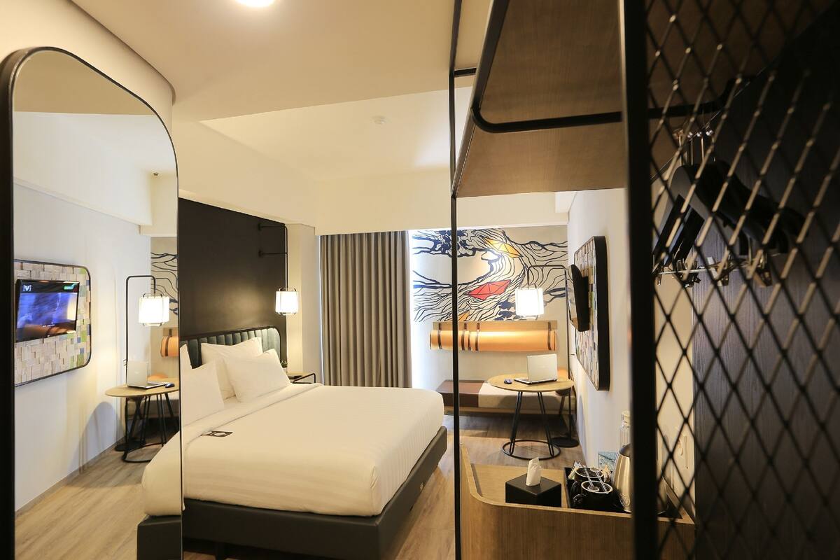 Habitación de hotel con una cama grande, un escritorio con una computadora portátil, un televisor en la pared y un cuadro decorativo.