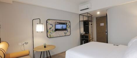 Quarto de hotel com uma cama, uma mesinha redonda com abajur, uma TV fixada na parede e um guarda-roupa.