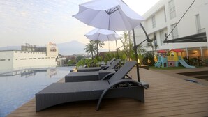Un espace aménagé au bord de la piscine, avec des chaises longues et des parasols, une aire de jeux pour enfants et un bâtiment portant une enseigne.