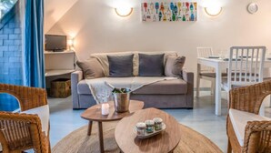 Un salon chaleureux avec un canapé, une table à manger, des chaises en osier, un téléviseur et un tableau accroché au mur.