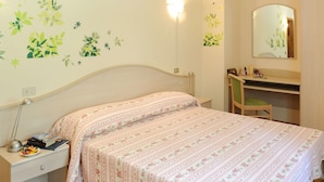A bedroom with a bed, bedside table, lamp, desk, chair, and mirror.