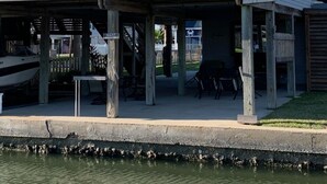 Una casa de dos pisos con un balcón, un muelle y una pequeña zona de estar al aire libre.