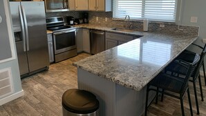 Una cocina moderna con electrodomésticos de acero inoxidable, encimera de granito y una ventana con persianas.