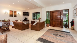 A living room with a sofa set, a dining table with chairs, a TV, and a large wooden door.