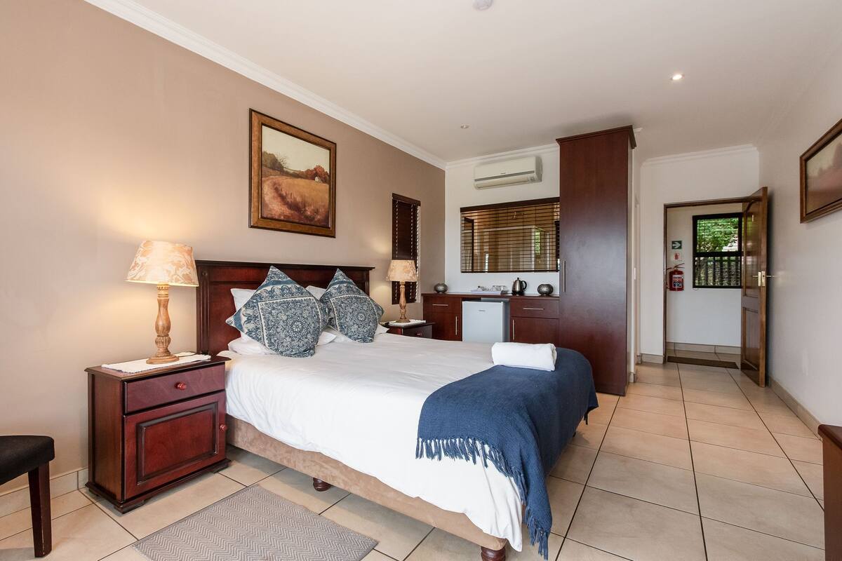 A bedroom with a bed, nightstands, a dresser, an air conditioning unit, and a door leading to another room.