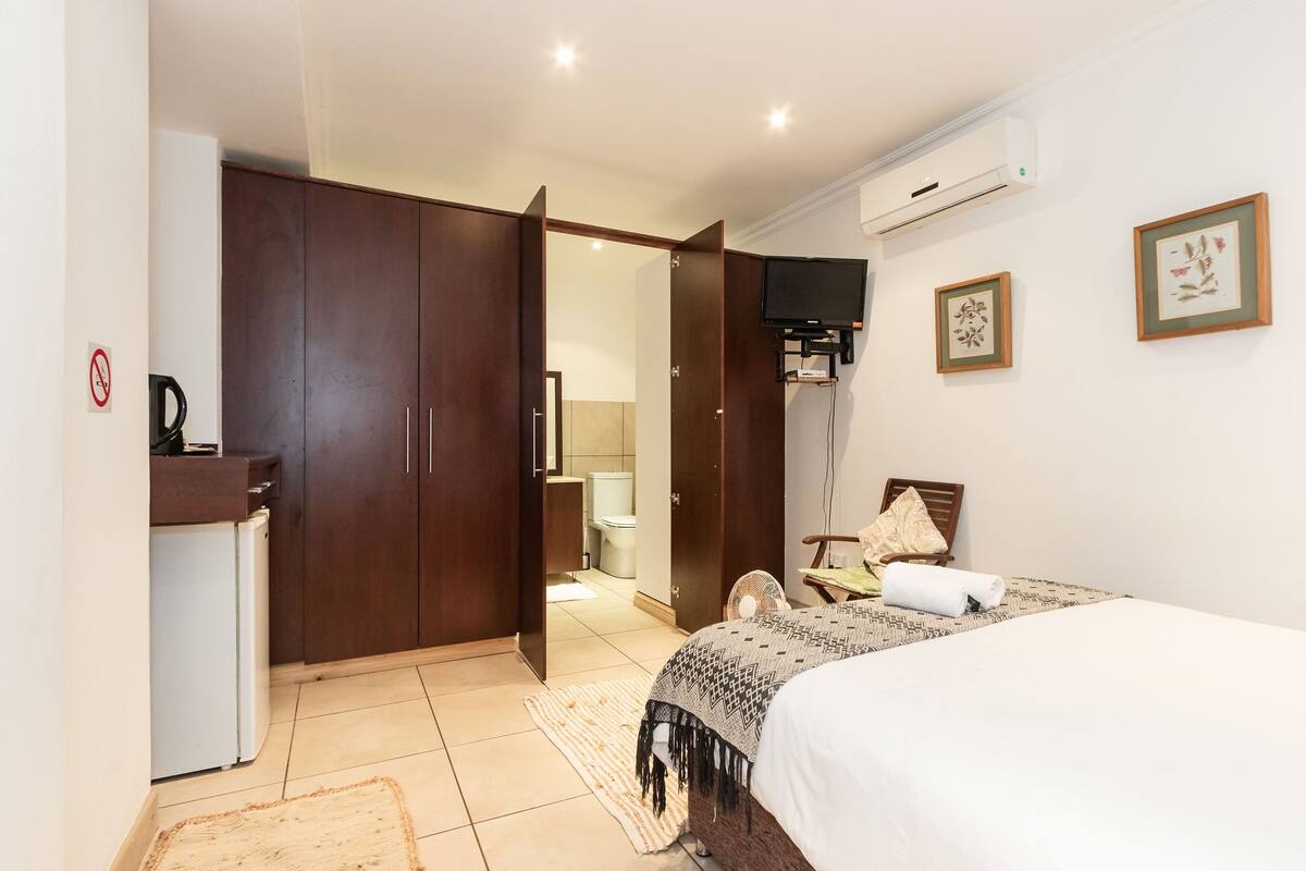 A hotel room with a bed, a wardrobe, a desk, a chair, and a television.