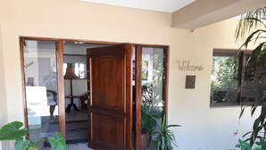 A wooden door leading to a room with a mirror, a welcome sign, and potted plants.