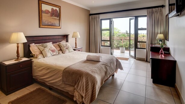 A bedroom with a large bed, two bedside tables with lamps, a painting on the wall, and a sliding glass door leading to a balcony.