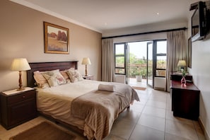 A bedroom with a large bed, two bedside tables with lamps, a painting on the wall, and a sliding glass door leading to a balcony. - Kites View Bed & Breakfast (Umhlanga)