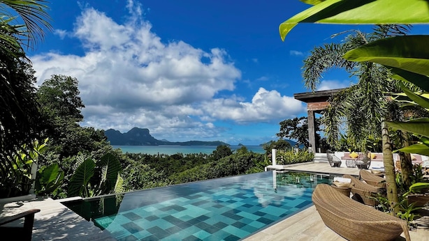 Una piscina infinita con agua azul cristalina, rodeada de plantas tropicales y vistas a las montañas y al mar.