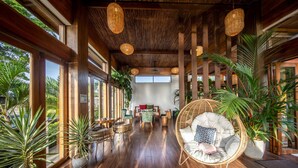 Una habitación amplia con pisos de madera, ventanas grandes y diversas opciones de asiento, incluyendo una silla de mimbre y un sofá.
