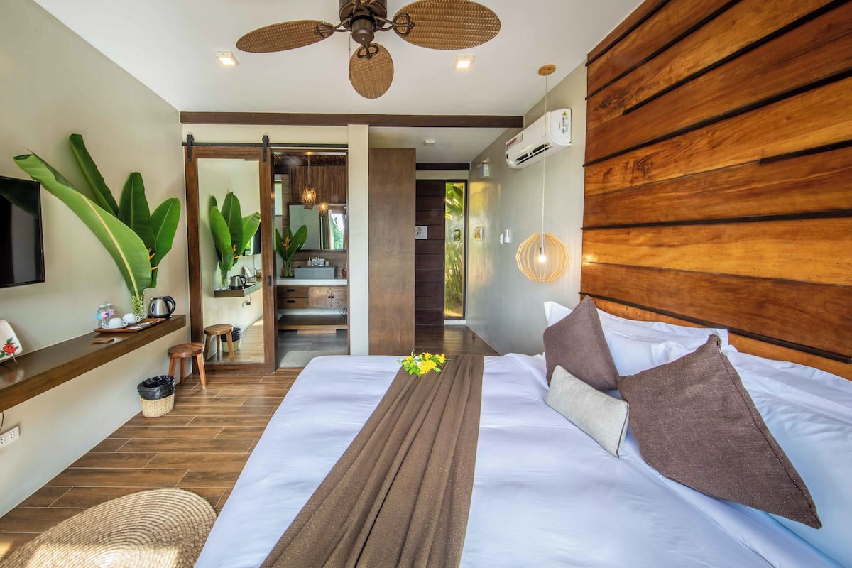 Una habitación de hotel moderna con una cama grande, cabecera de madera y un ventilador de techo.