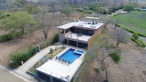 Una casa moderna de dos pisos con una gran piscina, un patio cubierto y vistas del paisaje circundante.