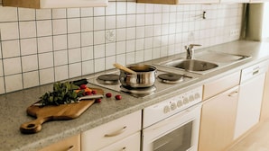 A kitchen with white cabinets, a tiled backsplash, a stove, a sink, and a cutting board with vegetables. - Lovely apartment for 6 guests with WIFI, TV and terrace (Thurmbach)
