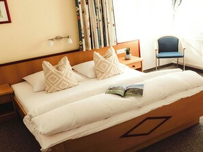 A double bed with patterned pillows, a bedside table with a lamp, a chair, and a window with curtains. - Cosy apartment for 6 people with WIFI, TV and terrace (Thurmbach)