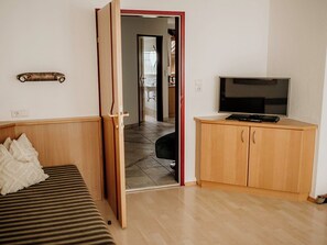 A room with a bed, a TV on a wooden cabinet, and a door leading to another room.