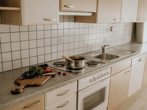 A kitchen with white cabinets, a tiled backsplash, a stove, and a sink. - Cosy apartment for 6 people with WIFI, TV and terrace (Thurmbach)